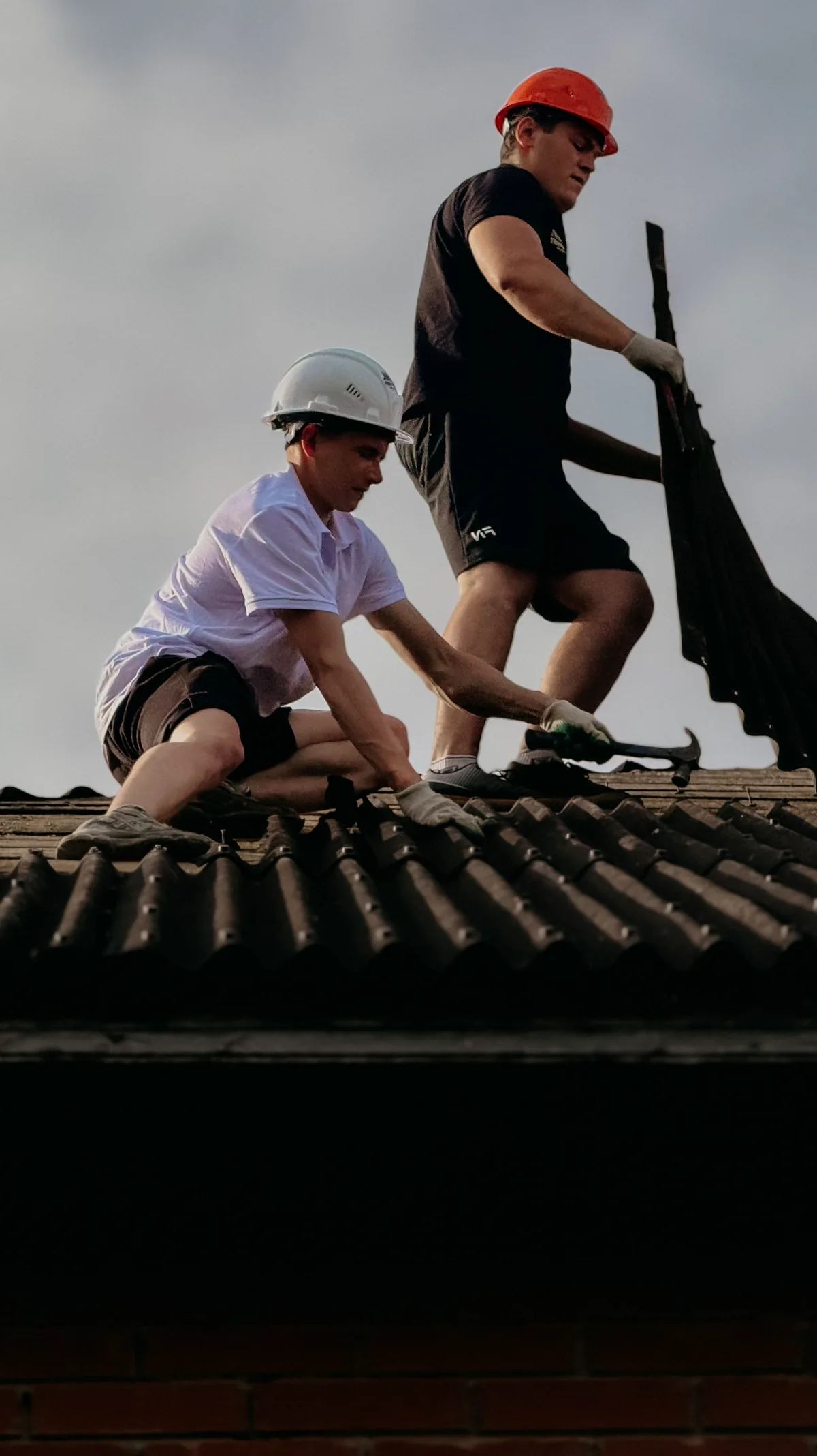 Dos operarios con casco trabajando sobre un tejado de teja, junto al borde del alero