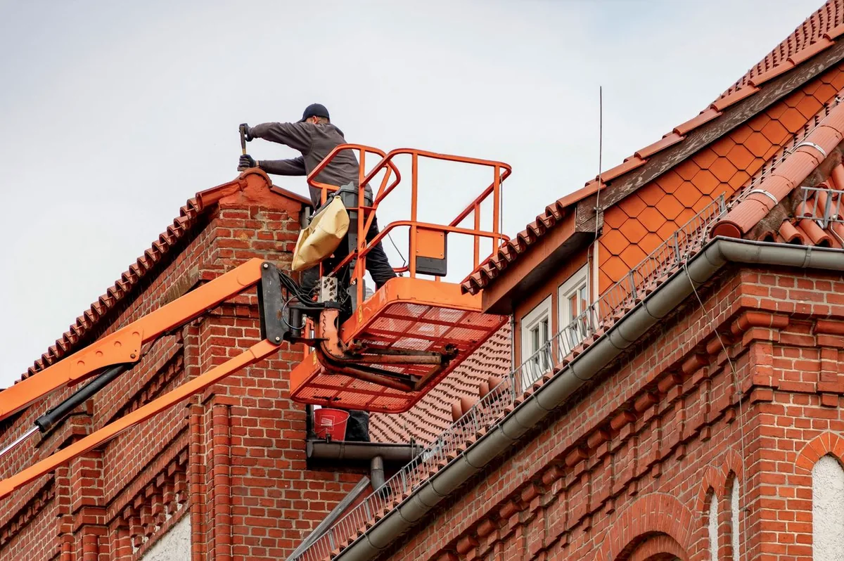 Operario trabajando desde la cesta de una plataforma elevadora sobre el remate de una cubierta