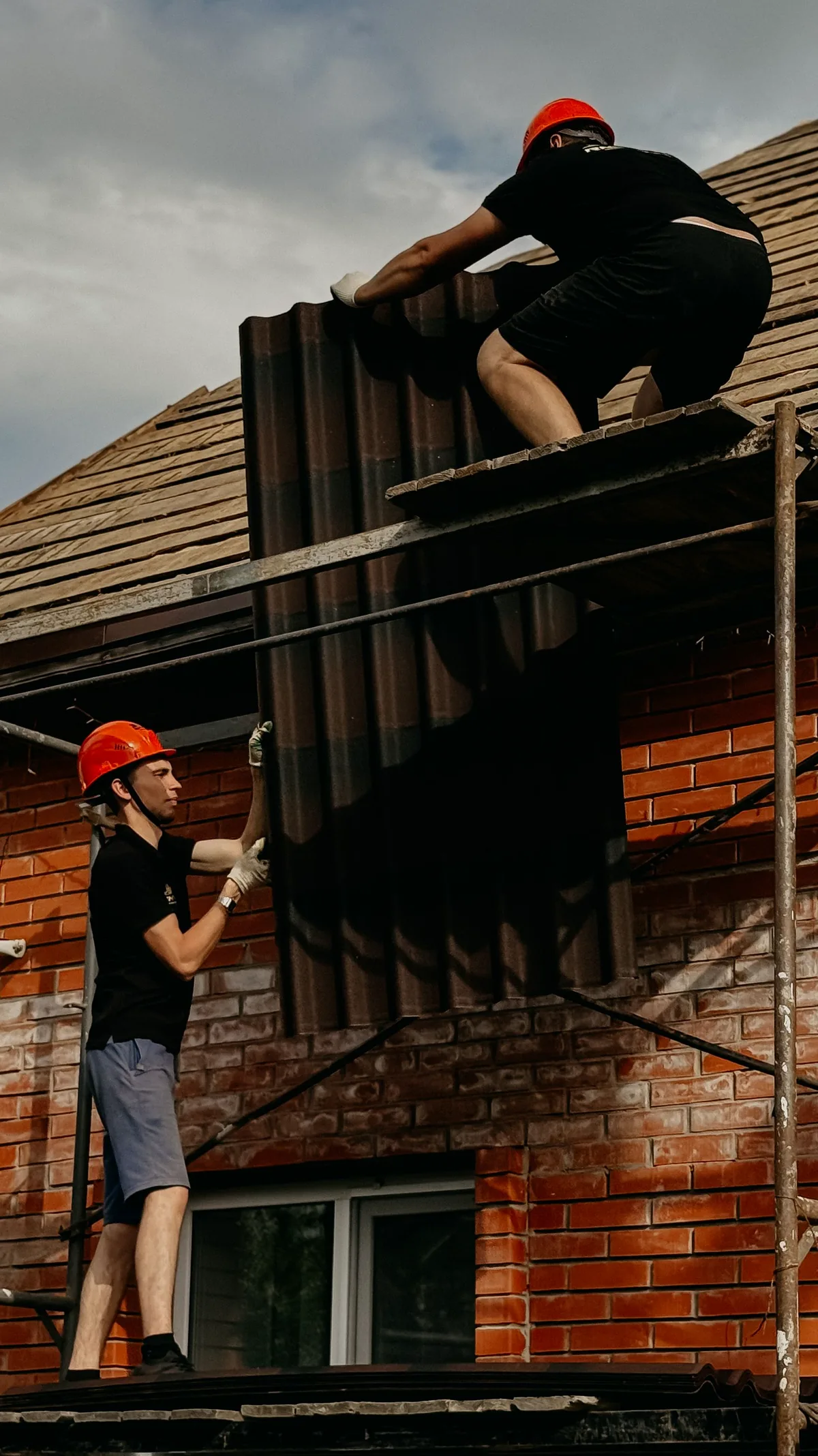 Dos operarios pasándose material de cubierta desde el faldón hasta el suelo